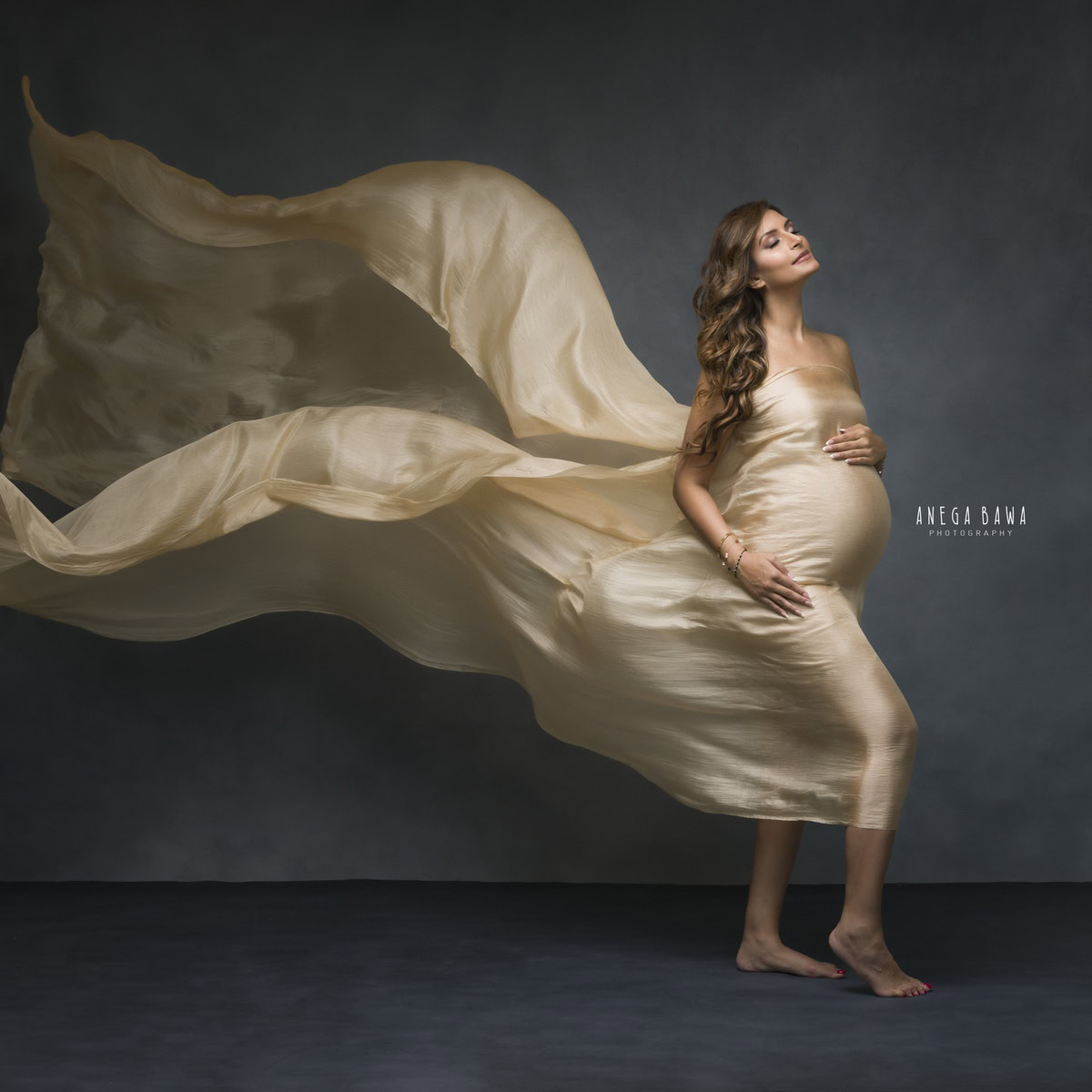 Best maternity shoot in Delhi with a mom-to-be in a golden wrap against a dark grey backdrop by Anega Bawa Photography, Gurgaon, Noida.