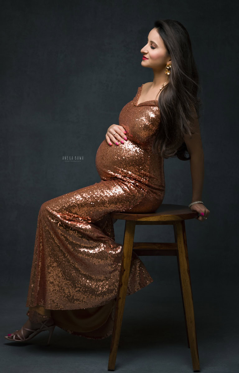 Maternity Photoshoot Delhi: Golden Shimmer Dress, Black Backdrop, Sitting Pose, by Anega Bawa Photography, Gurgaon Noida.