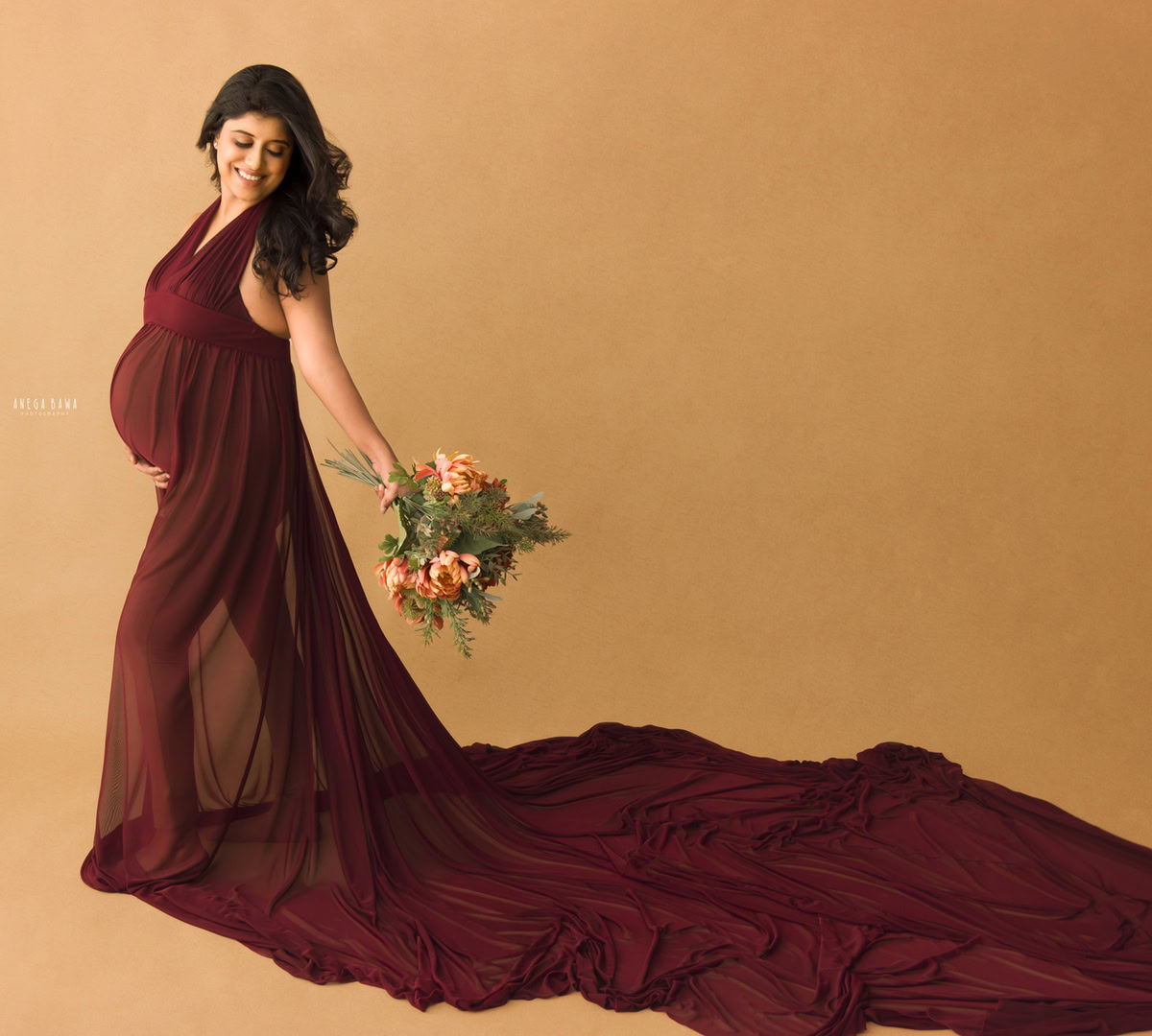 Maternity Shoot Delhi: Maroon Sleeveless Gown with Flowers, Beige Backdrop, by Anega Bawa Photography, Gurgaon Noida.