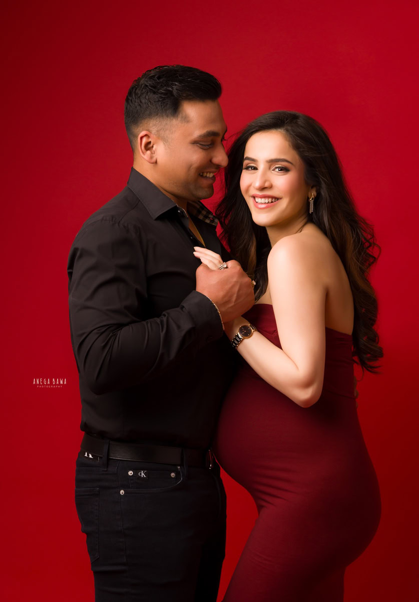 Pregnancy Photography in Delhi: Red Maroon Tube Gown with Spouse, Red Backdrop, by Anega Bawa, Photographer Gurgaon Noida.