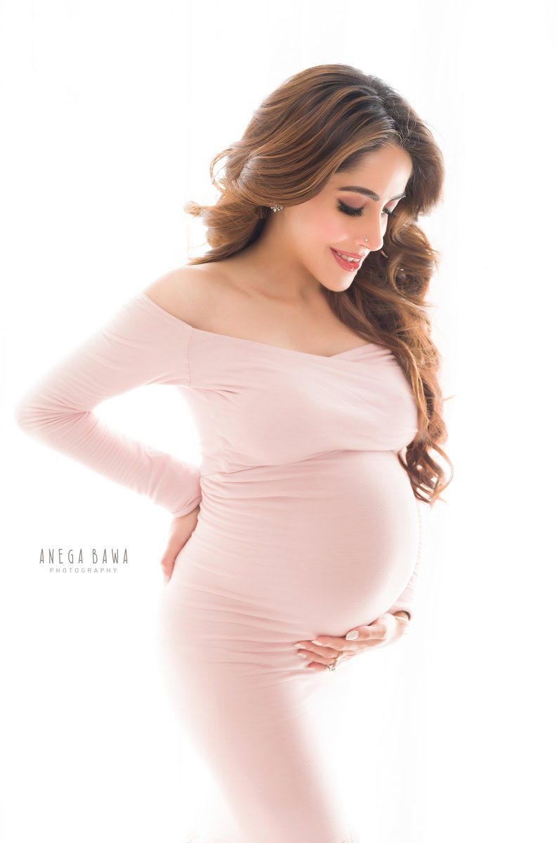 Elegant pregnant woman with long hair in soft pink dress, maternity photography, Anega Bawa Photography, portrait of expecting mother.