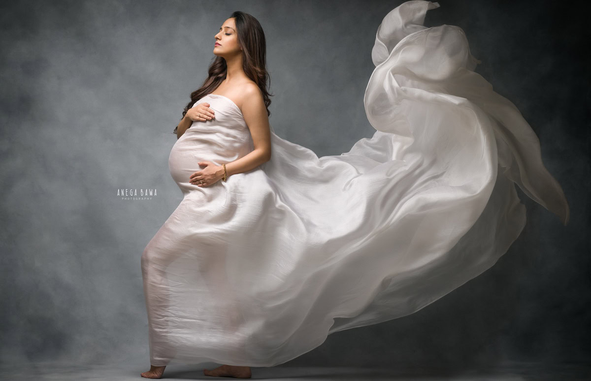 Pregnant woman maternity photography with flowing white fabric, artistic maternity pose, professional pregnancy photoshoot, elegant maternity portrait, Anega Bawa Photography.