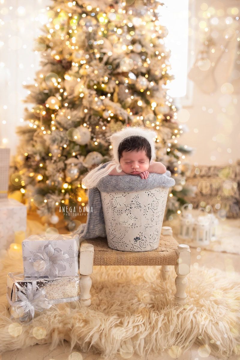 Newborn Photography in Delhi: Beige Rug, Xmas Tree with Golden Lights, White Cap, Cute Pose. Photographer: Anega Bawa, Gurgaon Noida.