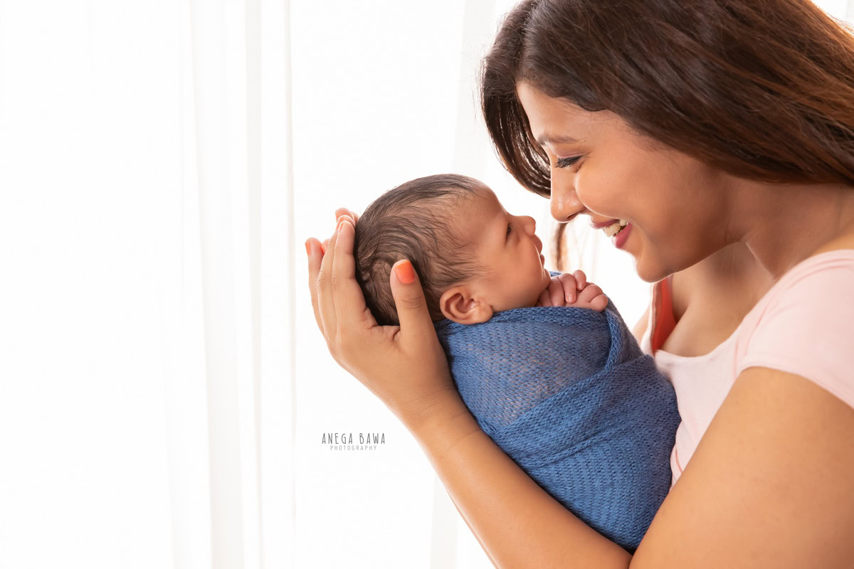 Newborn Photography in Delhi: A baby wrapped in blue with mom on a white backdrop. Photographer: Anega Bawa Photography, Gurgaon.