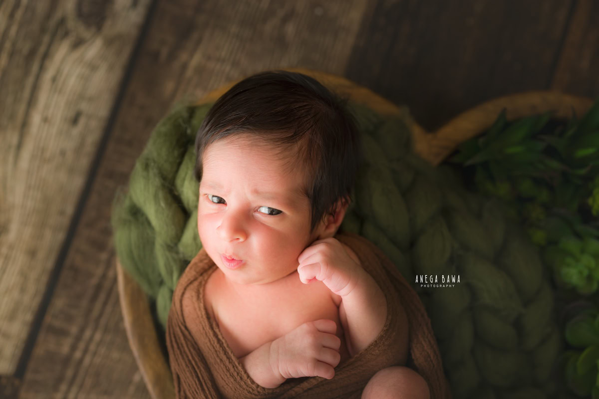 Newborn Photography in Delhi: Baby strikes a cute pout pose wrapped in brown against a brown backdrop. Captured by Anega Bawa during a photoshoot in Gurgaon Noida.
