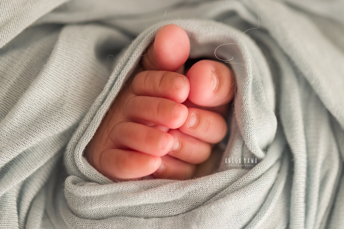 Newborn Photography in Delhi: Cute toes peeking out from a grey wrap, photographed by Anega Bawa in Gurgaon Noida.