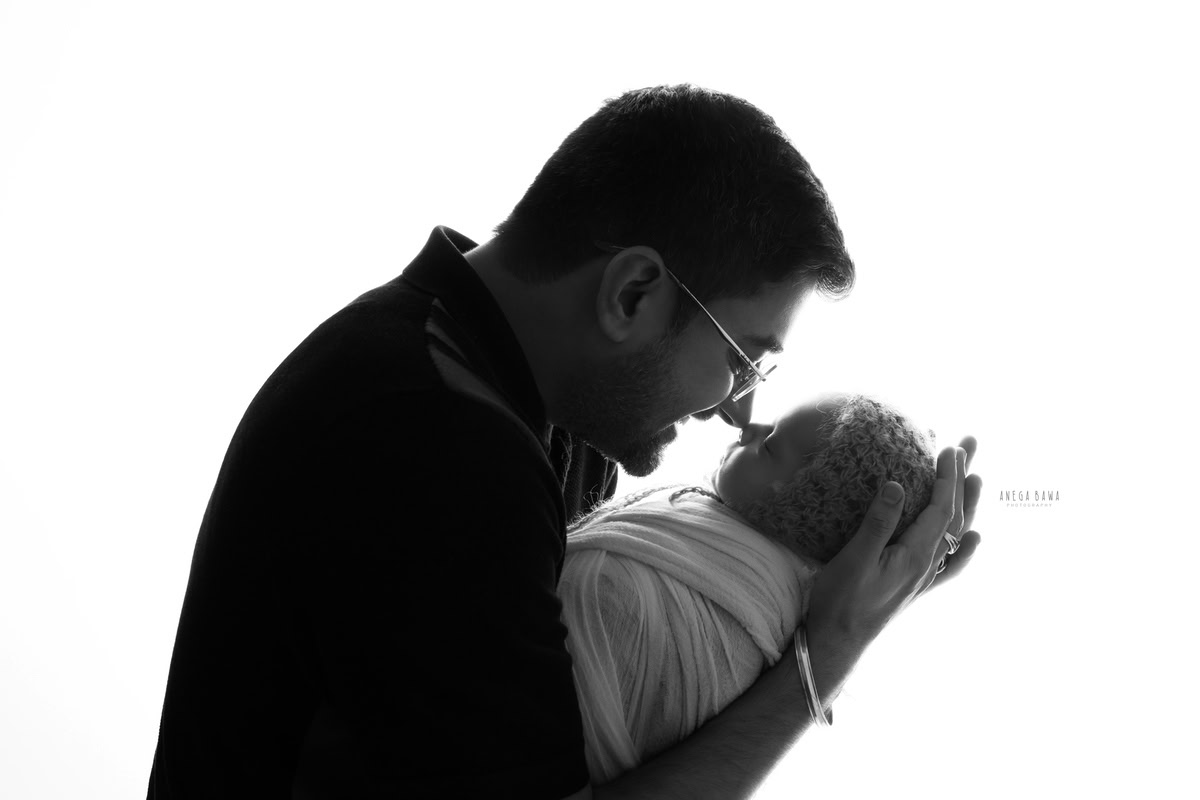 Newborn Photography in Delhi: Father and child captured in black and white against a white backdrop. Photographer: Anega Bawa Photography, Gurgaon.