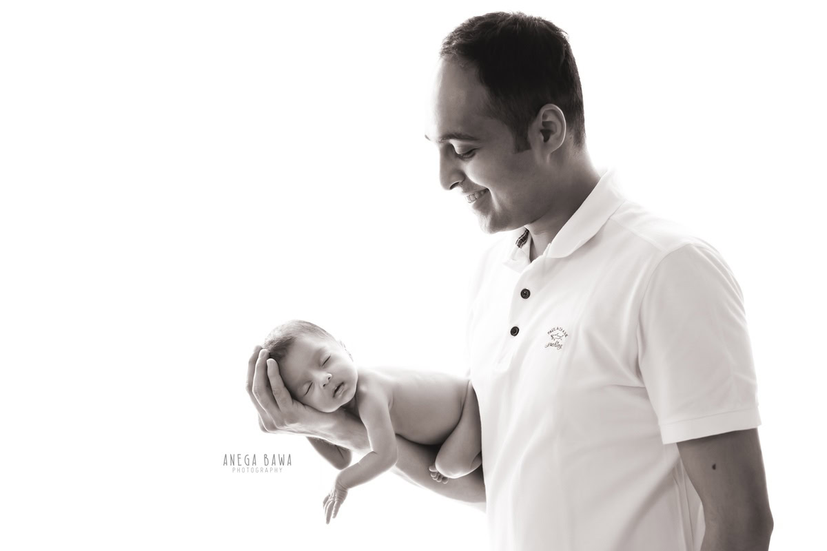 Newborn Photography in Delhi: Father posing in the Zara style with the newborn against a white backdrop. Photographer: Anega Bawa Photography, Gurgaon.