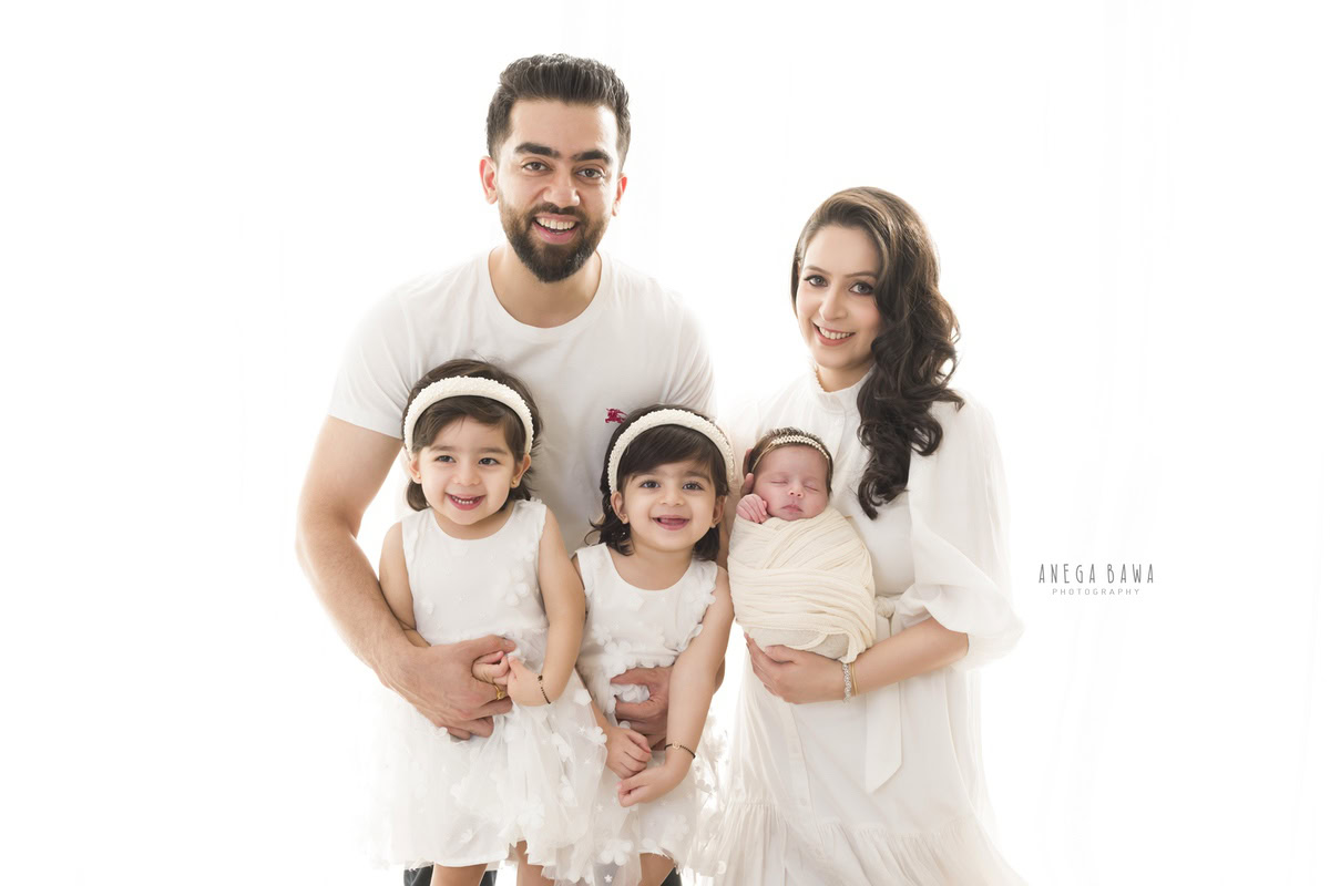 Newborn Photography in Delhi: Family captured in all-white attire against a white backdrop. Photographer: Anega Bawa Photography, Gurgaon.