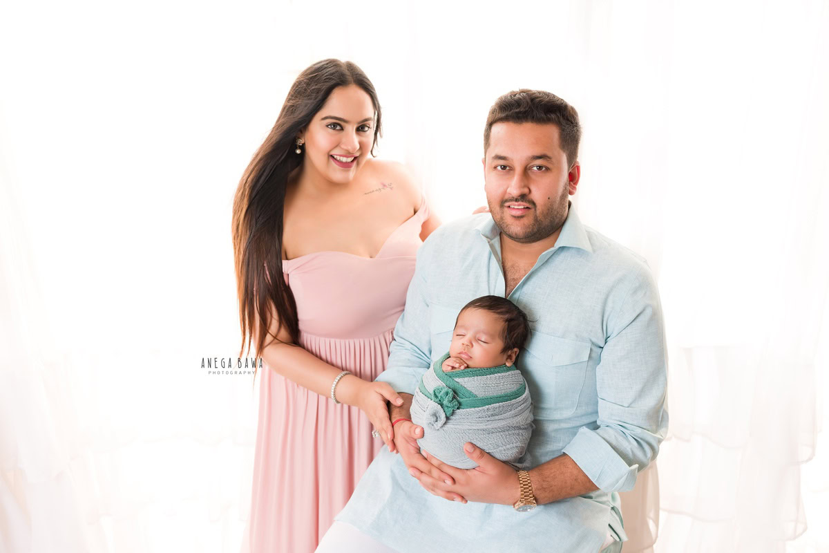 Newborn Photography in Delhi: Family posing with a grey-green wrap against a white backdrop, captured by Anega Bawa in Gurgaon.
