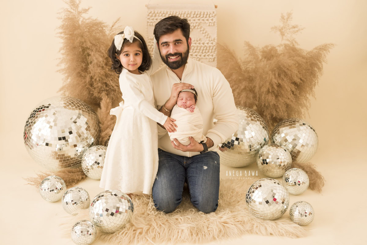 Newborn Photography in Delhi: Family captured in a smiling pose with a white wrap, photographed by Anega Bawa in Gurgaon.