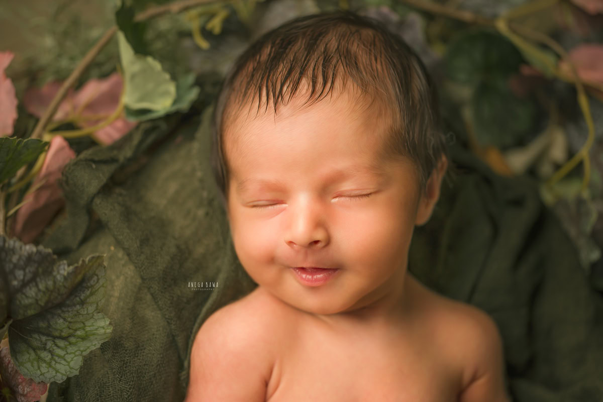Newborn Photography in Delhi: Green Backdrop, Capturing a Naughty Smile. Photographer: Anega Bawa Photoshoot, Gurgaon Noida.