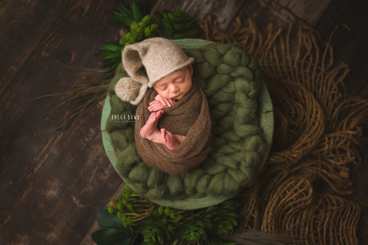 Newborn Photography in Delhi: Brown Wrap with Green Basket on Brown Backdrop. Photographer: Anega Bawa, Gurgaon Noida.