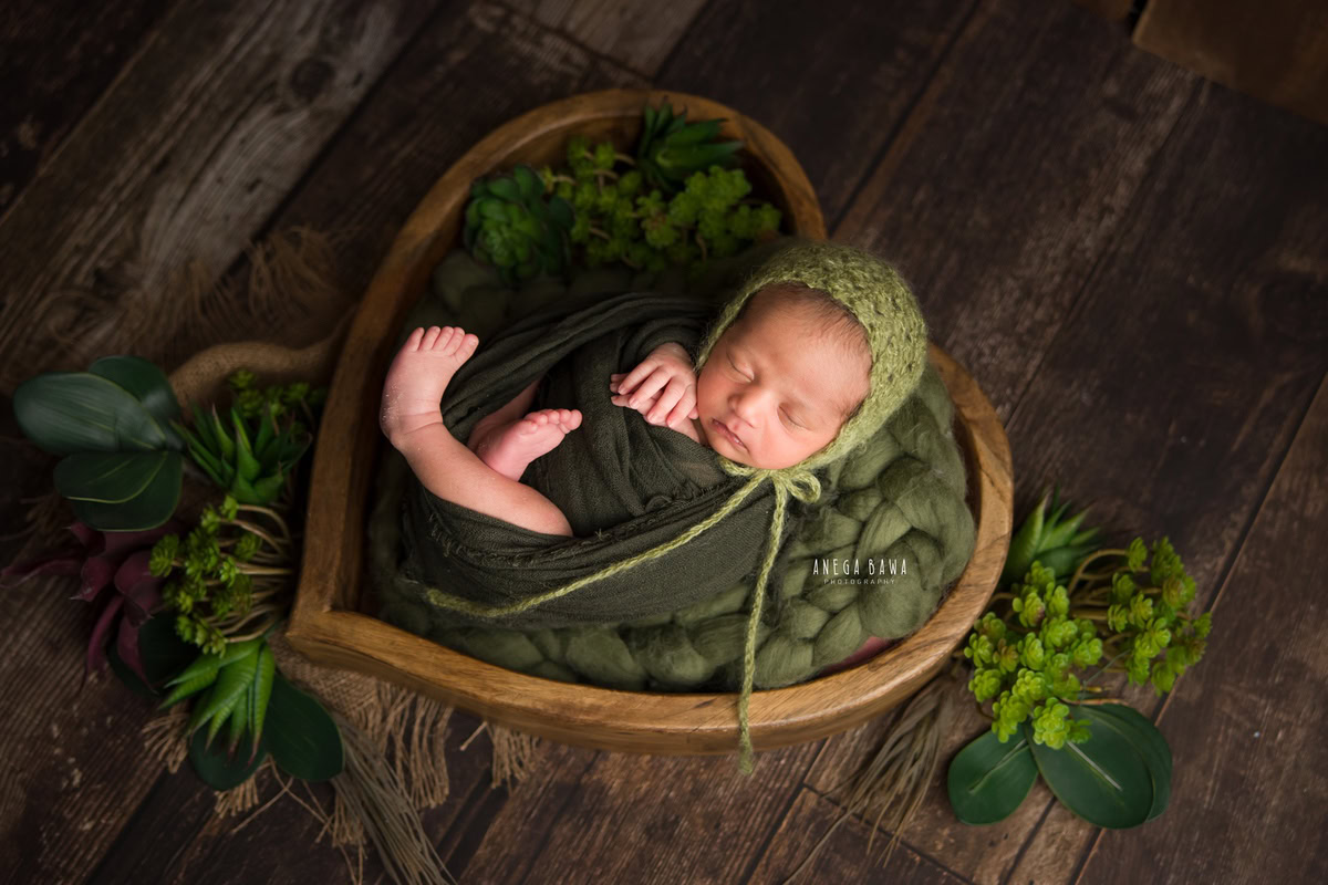 Newborn Photography in Delhi: Green Wrap, Heart-shaped Basket, Brown Backdrop. Photographer: Anega Bawa Photoshoot, Gurgaon Noida.