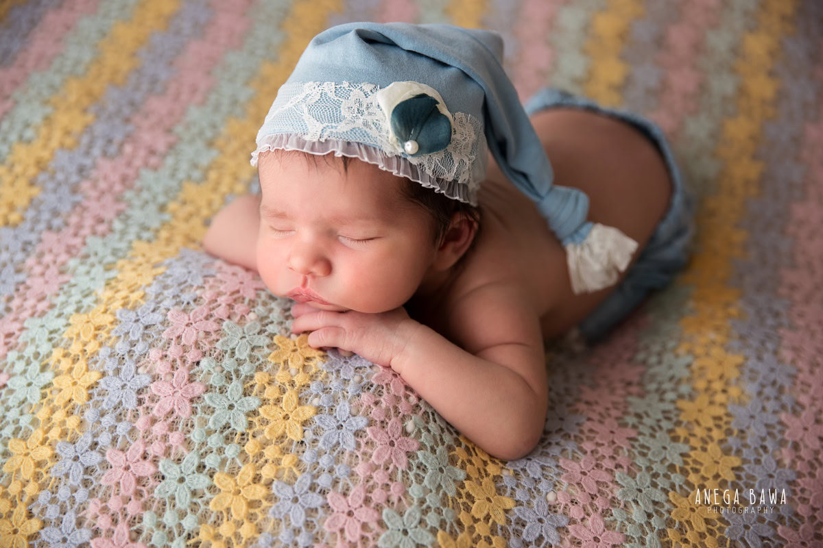 Newborn Photography in Delhi: Multicolour Baby Sheet, Cute Blue Cap, Lying Pose. Photographer: Anega Bawa Photoshoot, Gurgaon Noida.