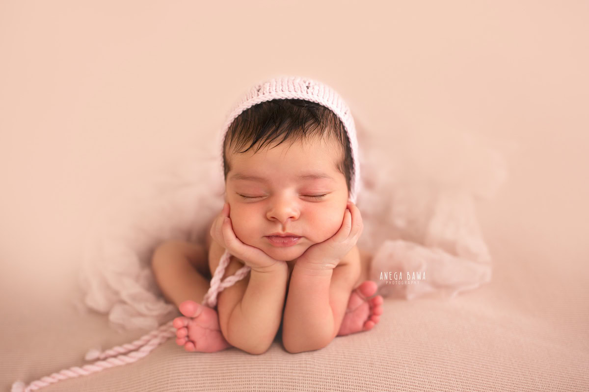 Newborn Photography in Delhi: Seated Pose with Pink Cap, Beige Backdrop. Photographer: Anega Bawa, Gurgaon Noida.