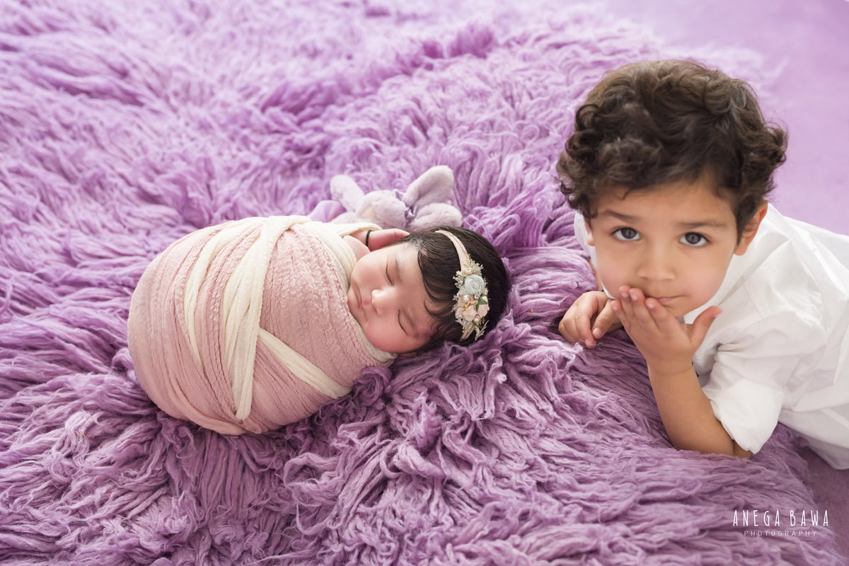 Newborn Photography in Delhi: Sibling Pose with Pink and White Wrap, Lavender Backdrop. Photographer: Anega Bawa, Gurgaon Noida.