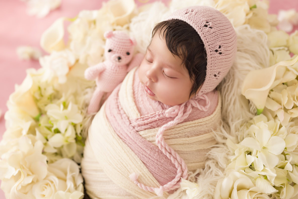 Newborn Photography in Delhi: Pink and white wrap adorned with white flowers, accompanied by a stuffed toy. Captured by Anega Bawa in Gurgaon Noida.