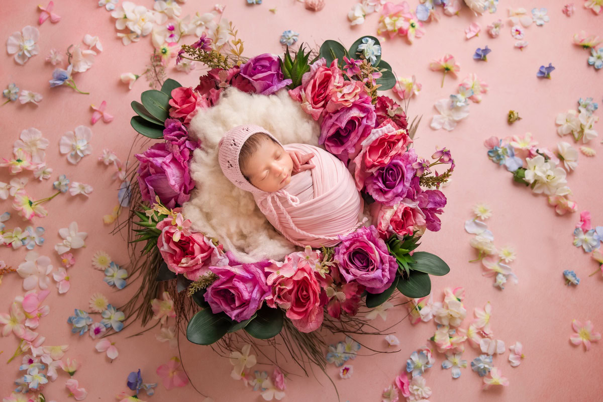 Newborn Photography in Delhi: A sleeping baby wrapped in pink with a floral basket and petals scattered on the floor. Photographer: Anega Bawa, Gurgaon Noida.