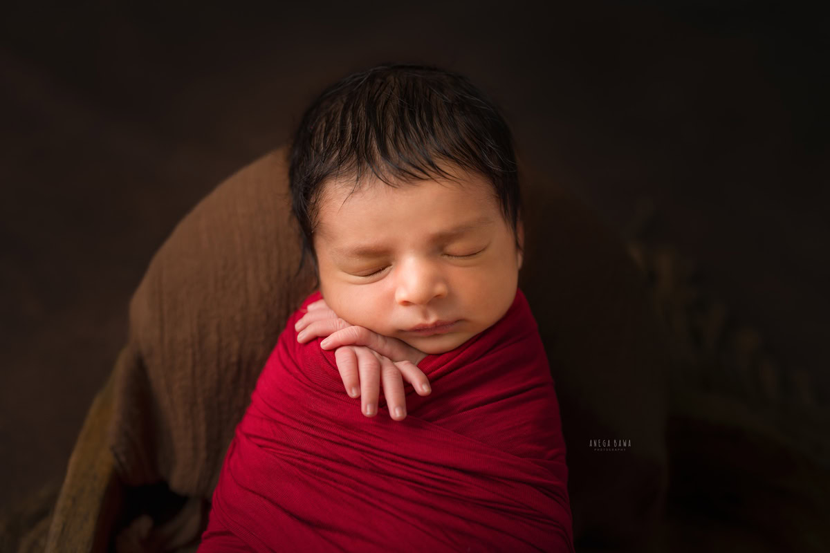 Newborn Photography in Delhi: Red Wrap with Brown Backdrop. Photographer: Anega Bawa, Gurgaon Noida.