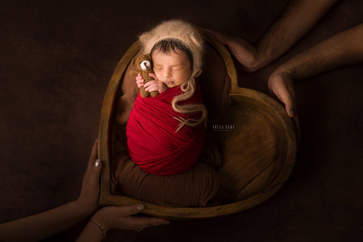 Newborn Photography in Delhi: Red Wrap with Soft Toy on Brown Backdrop. Photographer: Anega Bawa, Gurgaon Noida.