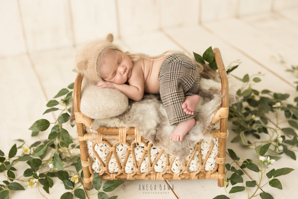 Newborn Photography in Delhi: Sleeping Pose on a Wooden Cot with Leaves on the Floor, Brown Cap. Photographer: Anega Bawa, Gurgaon Noida.