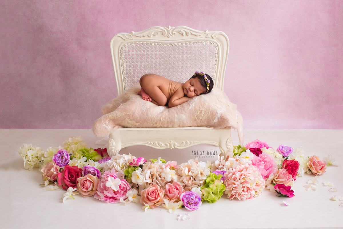 Newborn Photography in Delhi: White Wooden Chair, Pink Backdrop, Flowers on Floor. Photographer: Anega Bawa, Gurgaon Noida.
