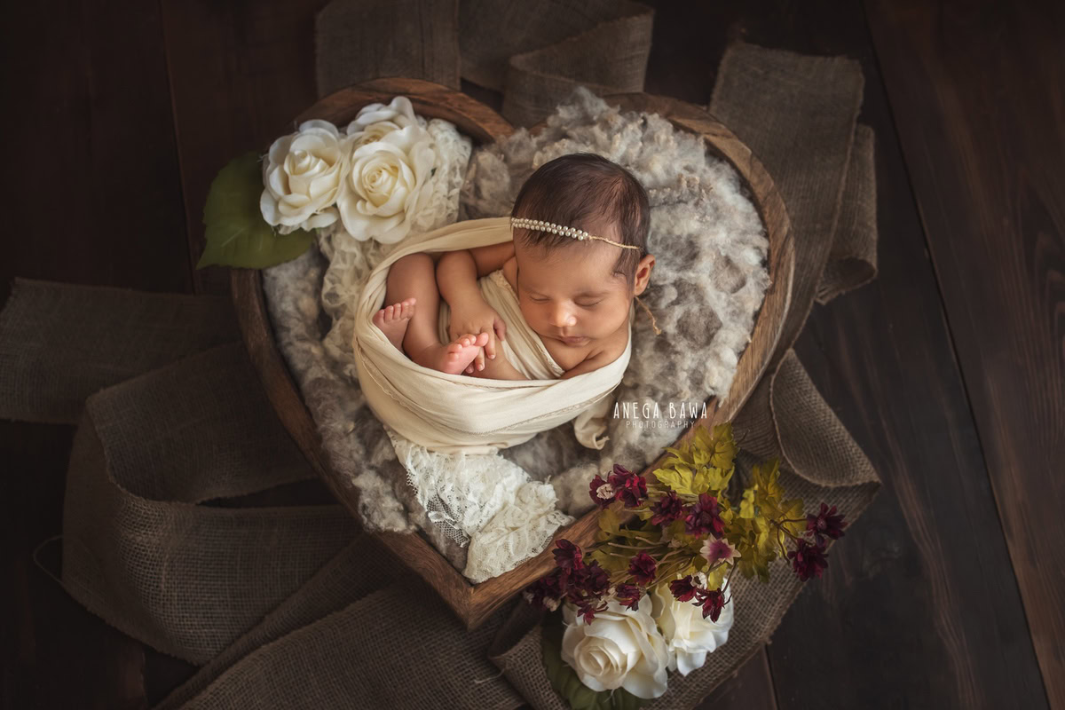 Newborn Photography in Delhi: White Wrap with Heart-shaped Basket and Pearl Headstring on Brown Backdrop. Photographer: Anega Bawa, Gurgaon Noida.