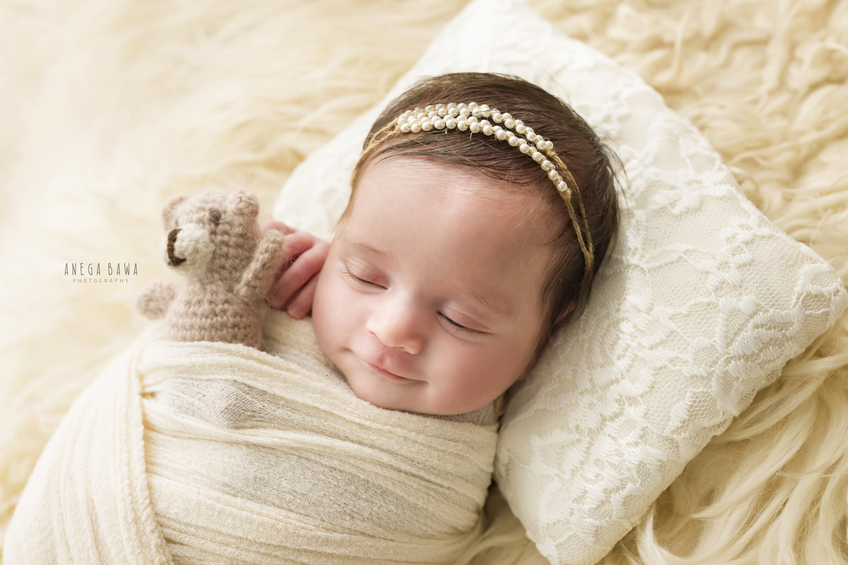 Newborn Photography in Delhi: White Wrap, Soft Toy, Beige Rug, Cute Smiling Pose. Photographer: Anega Bawa, Gurgaon Noida.