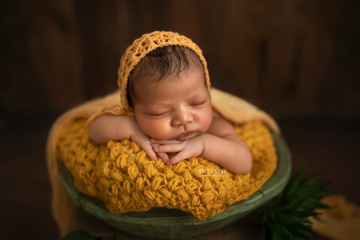 Newborn Photography in Delhi: Yellow Cap, Green Basket, Brown Backdrop. Photographer: Anega Bawa, Gurgaon Noida.