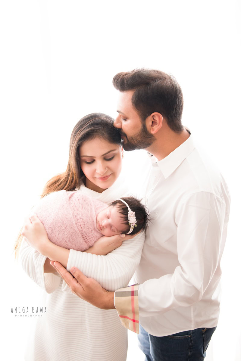 Newborn Photography in Gurgaon: Family with newborn wrapped in pink against a white backdrop. Photographer: Anega Bawa, Delhi.