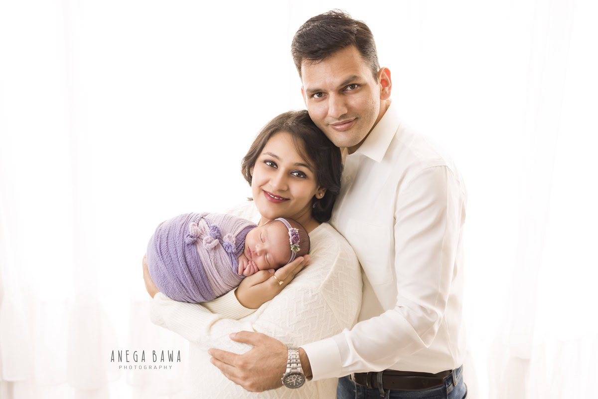 Newborn Photography in Gurgaon: Family portrait with newborn wrapped in purple mauve, against a white backdrop. Photographer: Anega Bawa, Delhi.