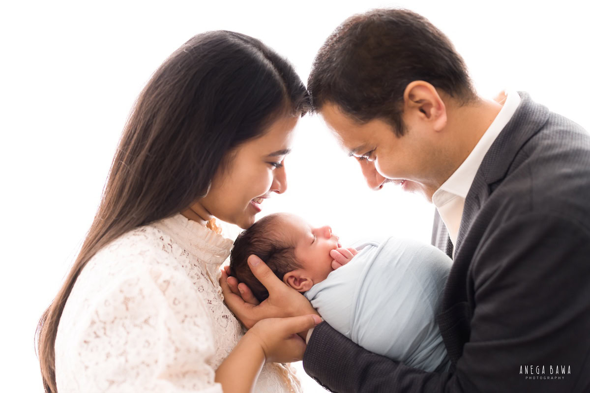 Newborn Photography in Gurgaon: Family portrait with newborn wrapped in sky blue against a white backdrop. Photographer: Anega Bawa, Delhi.