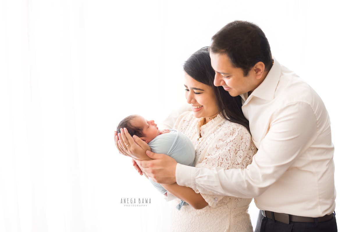 Newborn Photography in Gurgaon: Family portrait with newborn wrapped in sky blue against a white backdrop. Photographer: Anega Bawa, Delhi.