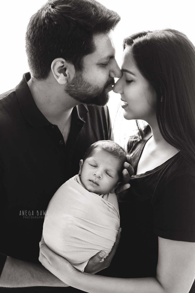 Newborn Photography in Gurgaon: Family portrait with newborn wrapped in white against a black and white backdrop. Photographer: Anega Bawa, Delhi.