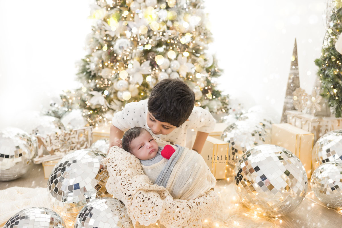 Newborn Photoshoot in Delhi: Blue and White Wrap with Xmas Tree and Sibling, White Backdrop with Disco Ball. Photographer: Anega Bawa Photography, Gurgaon Noida.