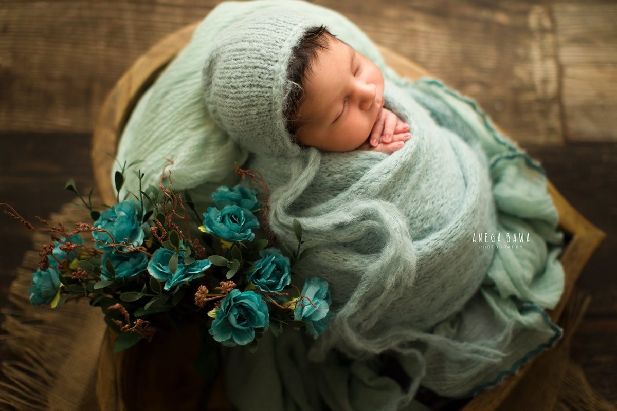 Newborn Photoshoot in Delhi: Baby wrapped in blue with blue flowers against a brown backdrop. Photographer: Anega Bawa, Gurgaon Noida.