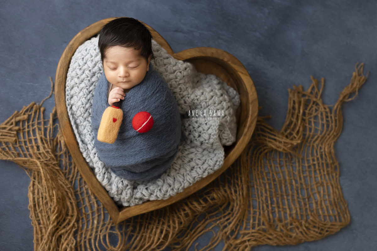 Newborn Photoshoot in Delhi: Brown Basket with Blue Wrap and Bat Ball on Blue Backdrop. Photographer: Anega Bawa Photography, Gurgaon Noida.