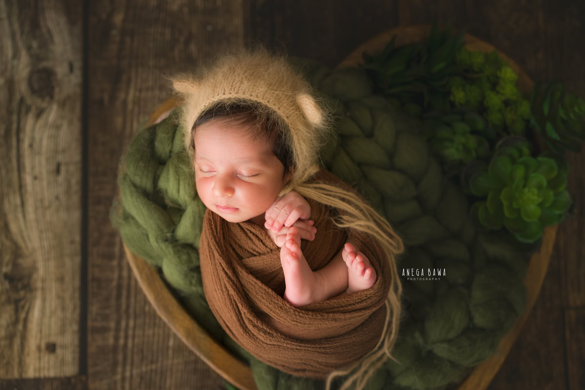 Newborn Photoshoot in Delhi: A baby wrapped in brown fabric with a matching cap against a brown backdrop. Photographer: Anega Bawa Photography, Gurgaon Noida.