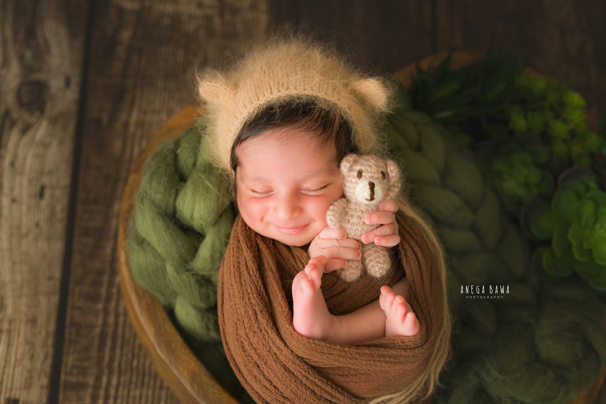 Newborn Photoshoot in Delhi: Brown Wrap, Soft Toy, Brown Backdrop, Capturing a Smiling Pose. Photographer: Anega Bawa Photography, Gurgaon Noida.