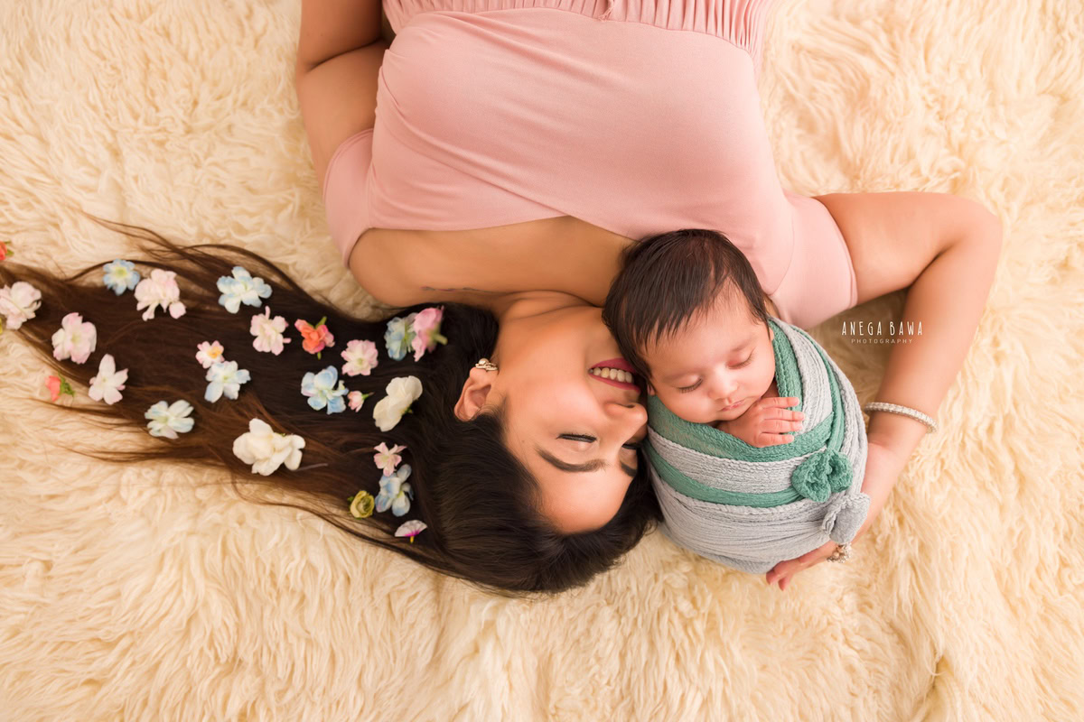 Newborn Photoshoot in Delhi: Mom sitting on a beige rug, holding her baby wrapped in a grey-green wrap. Photographer: Anega Bawa Photography, Gurgaon.