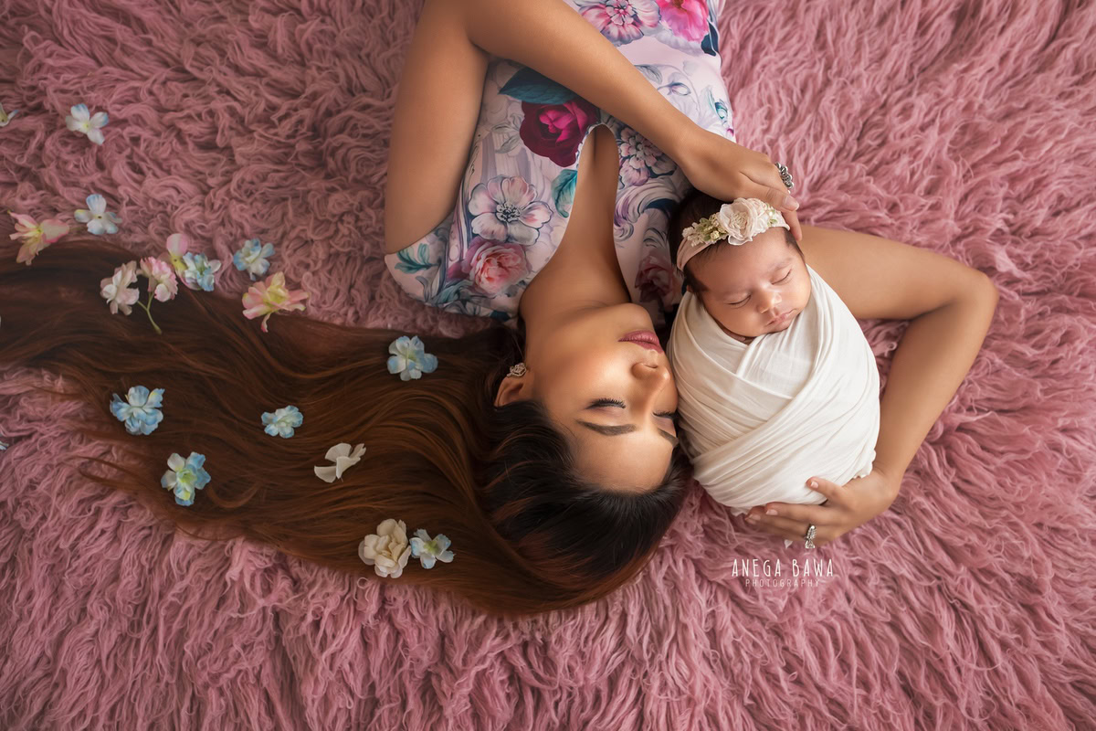 Newborn Photoshoot in Delhi: Mom holding her newborn on a pink rug, wrapped in white, with a cute headband. Photographer: Anega Bawa Photography, Gurgaon.