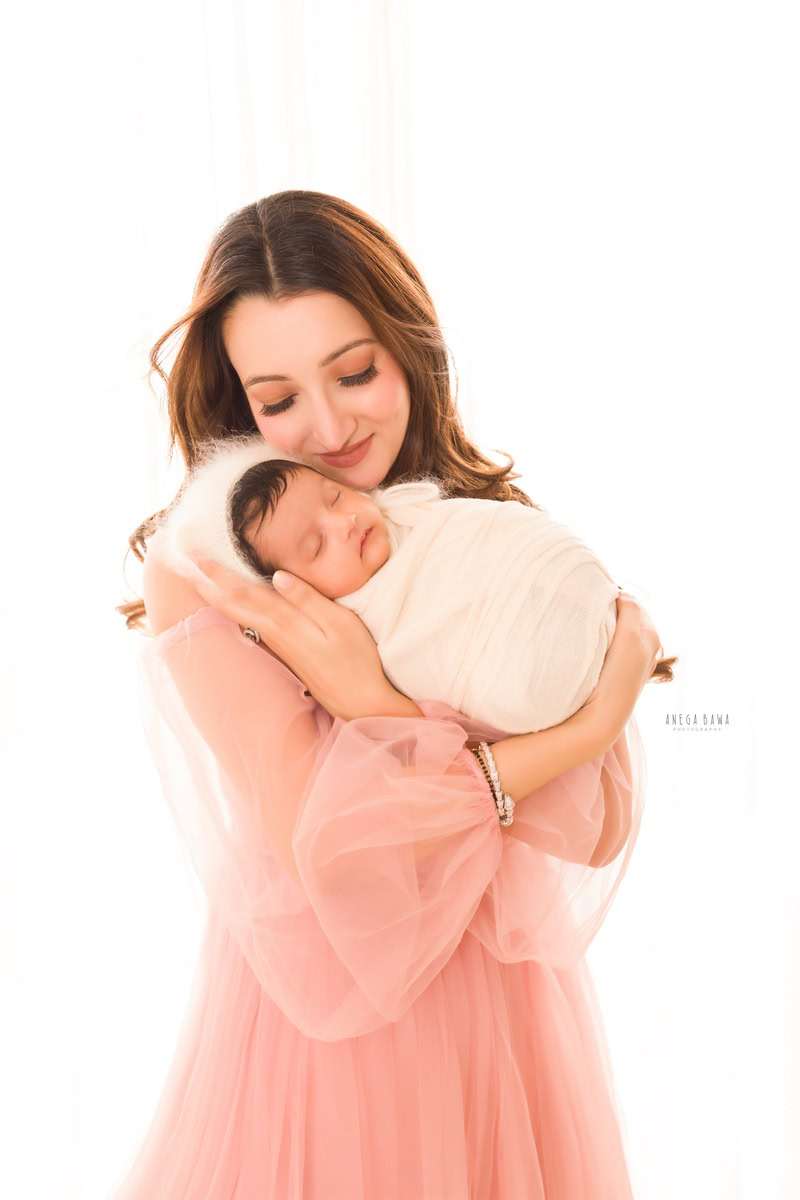 Newborn Photoshoot in Delhi: Mom holding baby in a white wrap, capturing a sweet pose against a white backdrop. Photographer: Anega Bawa Photography, Gurgaon.
