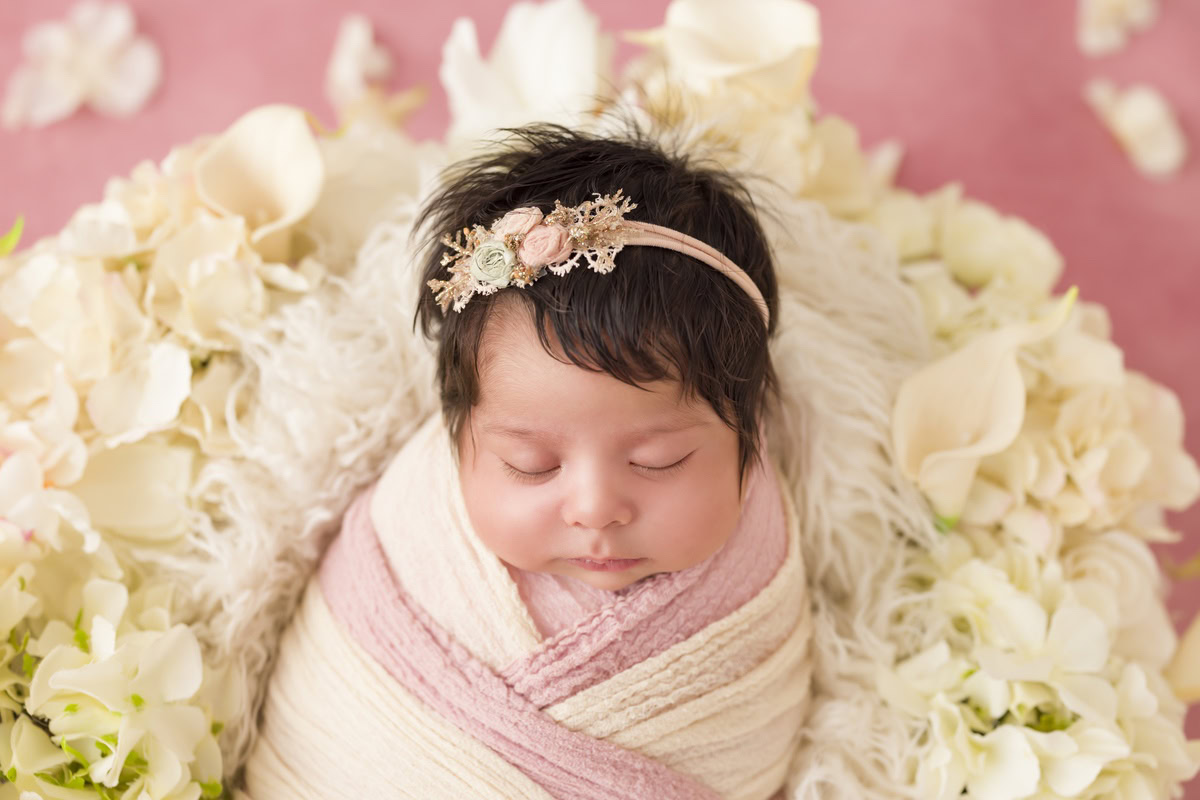 Newborn Photoshoot in Delhi: Pink Backdrop with Pink and White Wrap and White Flowers. Photographer: Anega Bawa Photography, Gurgaon Noida.