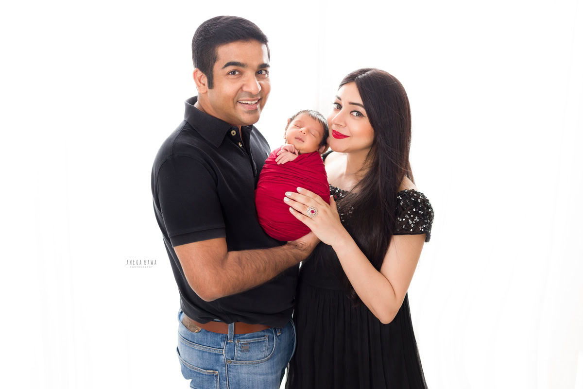 Newborn Photoshoot in Delhi: Family with newborn wrapped in red against a white backdrop. Photographer: Anega Bawa Photography, Gurgaon.