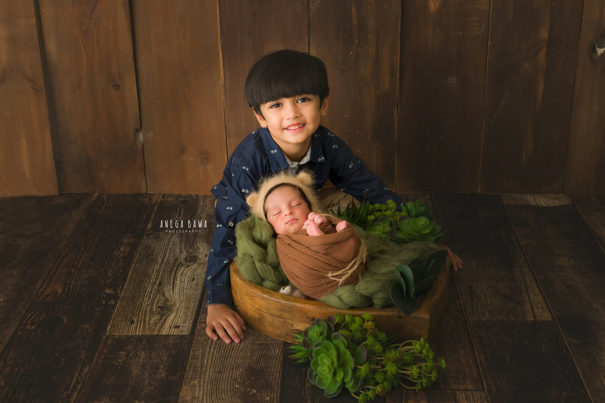 Newborn Photoshoot in Delhi: Sibling Pose with Brown Wrap on Wooden Floor. Photographer: Anega Bawa Photography, Gurgaon Noida.