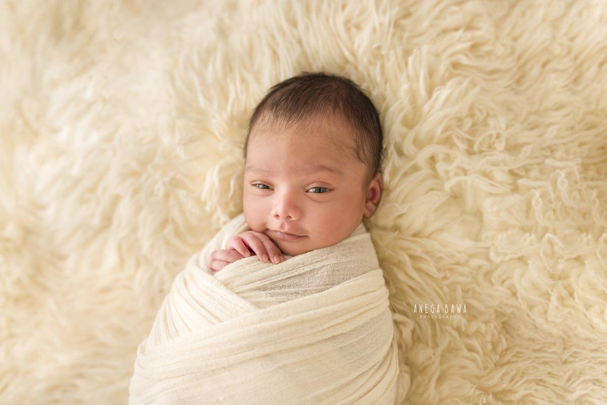 Newborn Photoshoot in Delhi: White Wrap with Naughty Eyes, Beige Backdrop. Photographer: Anega Bawa, Gurgaon Noida.