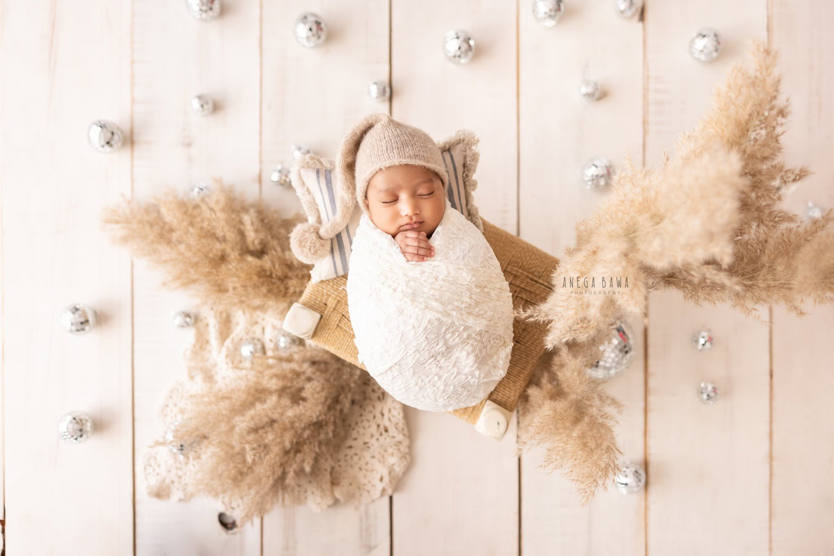 Newborn Photoshoot in Delhi: White Wrap with Pampas and Silver Balls, Sleeping Pose, White Backdrop. Photographer: Anega Bawa, Gurgaon Noida.