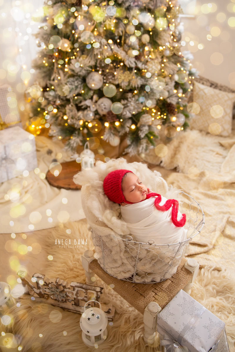 Newborn Photoshoot in Delhi: White Wrap with Red Cap, Xmas Tree, Golden Lights. Photographer: Anega Bawa, Gurgaon Noida.