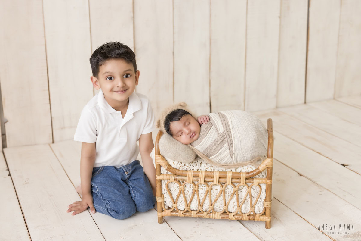 Newborn Photoshoot in Gurgaon: Beige and White Wrap with Wooden Cot and Sibling. Photographer: Anega Bawa, Delhi Noida.